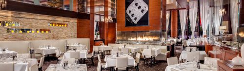 Upscale restaurant dining room with white tablecloths, modern fireplace, and elegant décor.