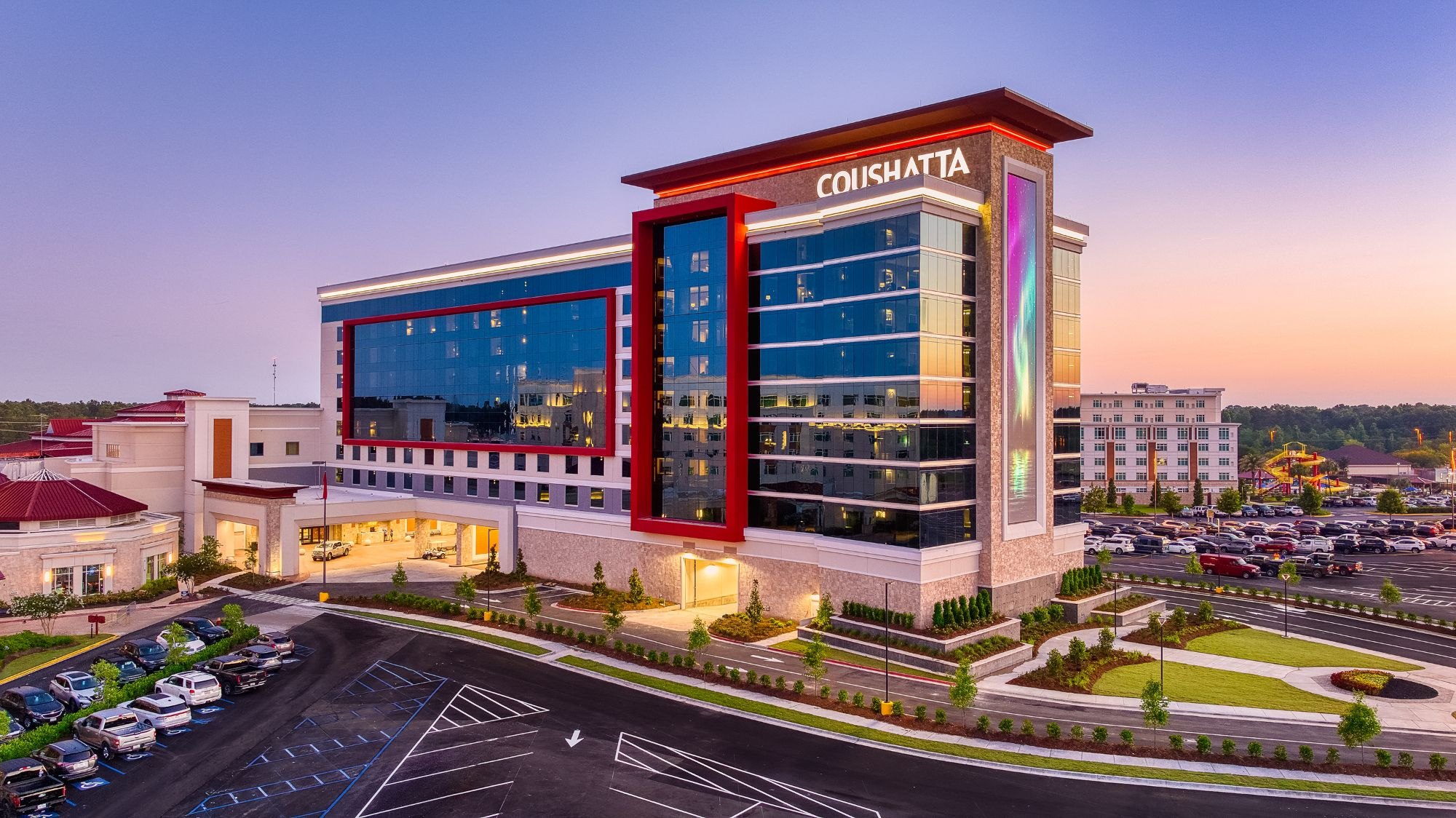 The Coushatta hotel tower at dusk, with its glass facade, red frame and lit Coushatta sign above the entrance
