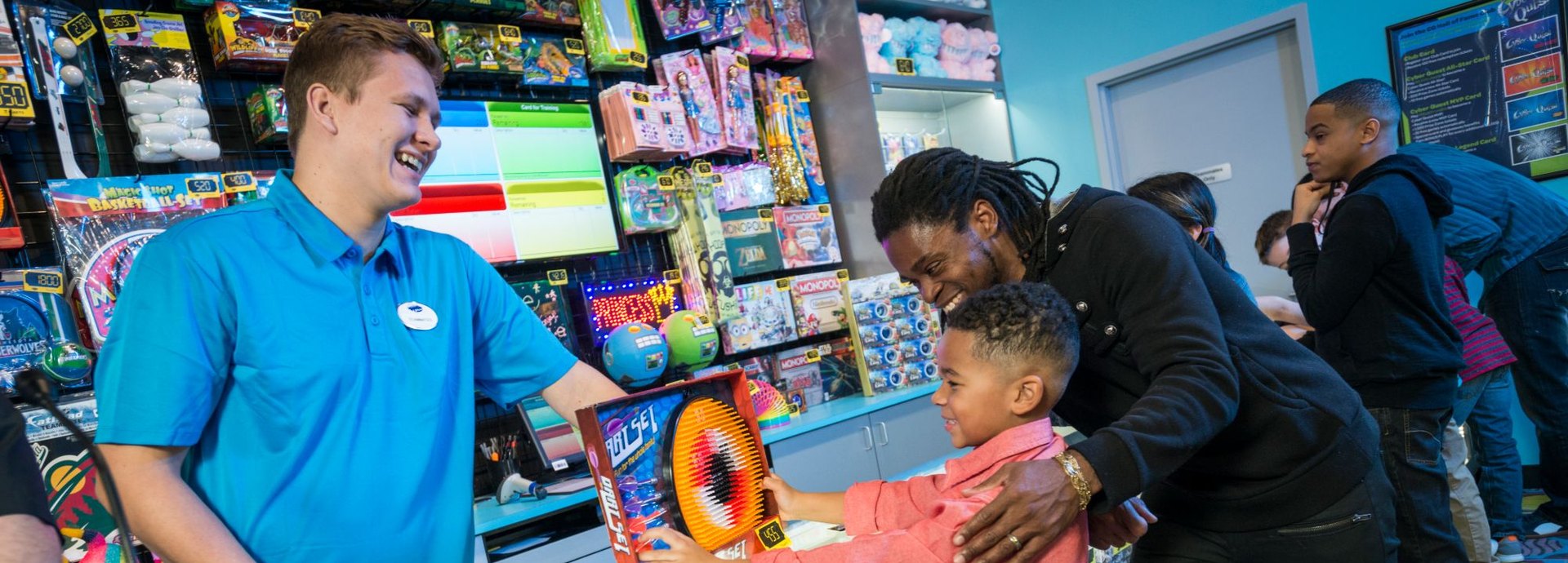 A boy and his dad pick out a prize with a Cyber Quest teammate at the Prize Zone counter