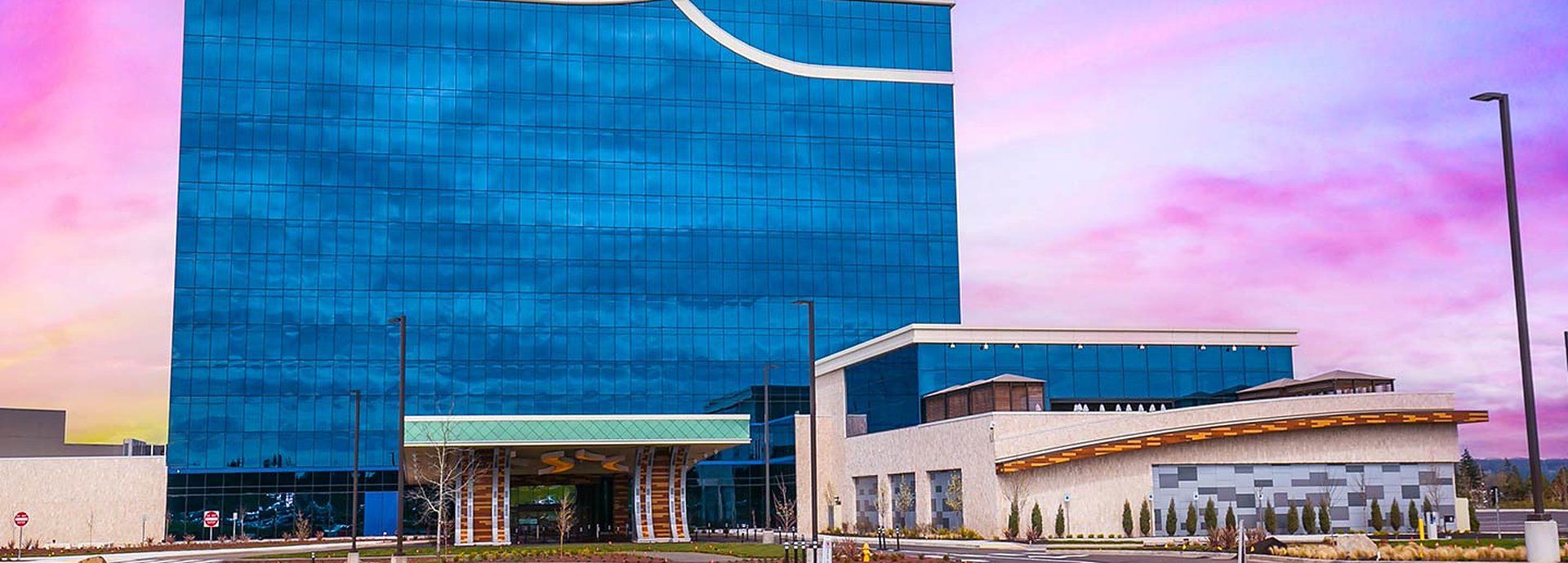 The blue glass hotel tower and entrance at ilani in Ridgefield, Washington, under a pink sunset sky