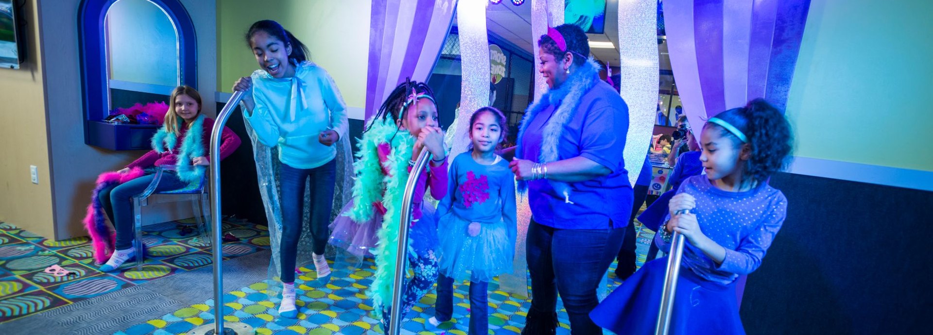 Kids in feather boas and tutus perform on the Star Stage with a Kids Quest teammate
