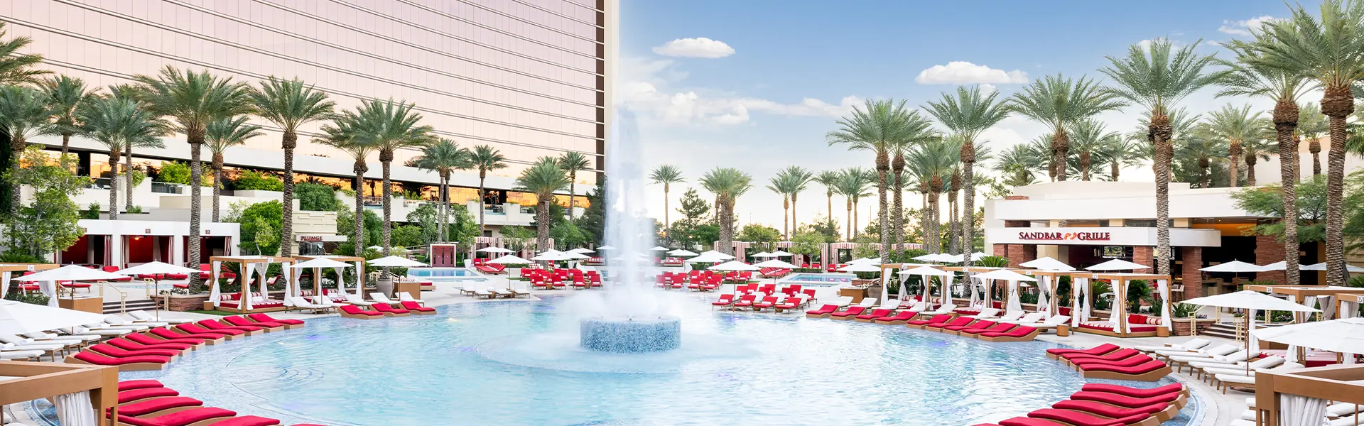 The pool at Red Rock Casino Resort & Spa in Las Vegas, with a tall fountain, red loungers, white cabanas and palm trees