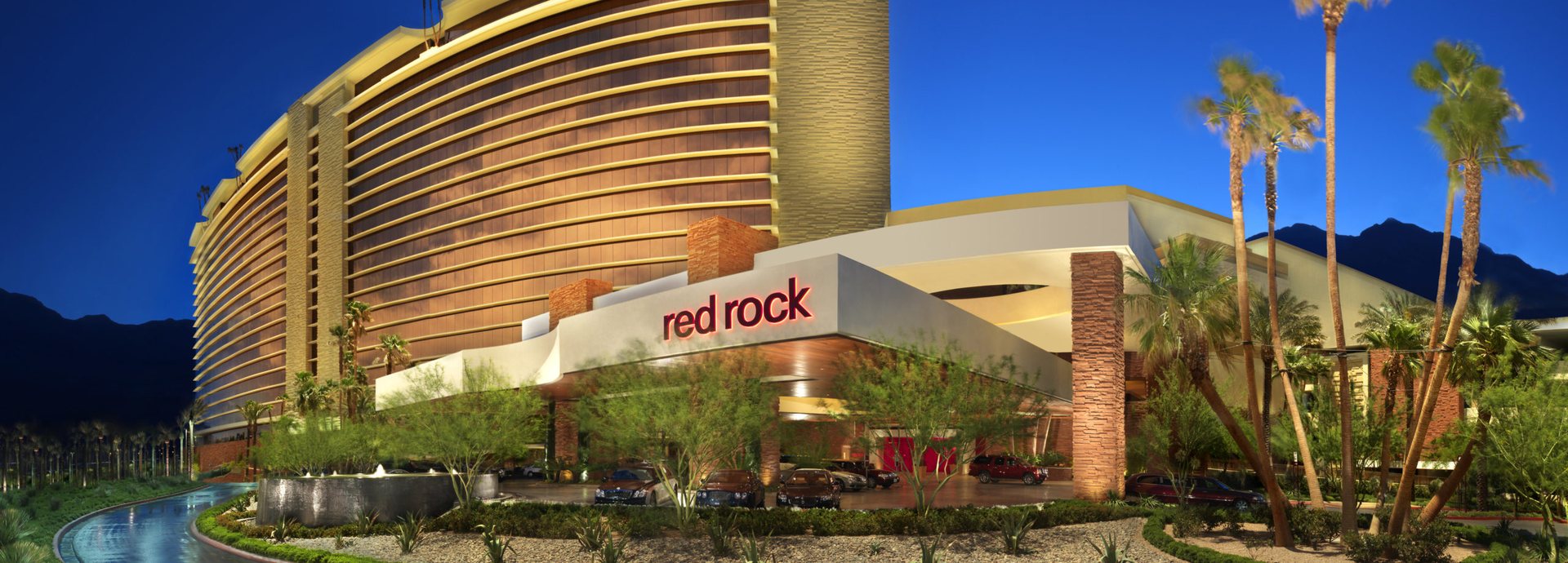 Red Rock Casino Resort & Spa in Las Vegas at dusk, with its curved hotel tower, red rock sign and palm-lined entrance