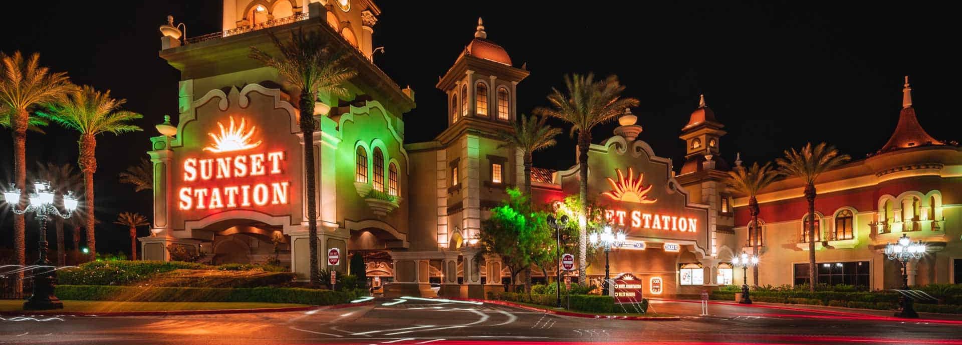 The Sunset Station entrance towers and signs lit up at night among palm trees in Henderson, Nevada