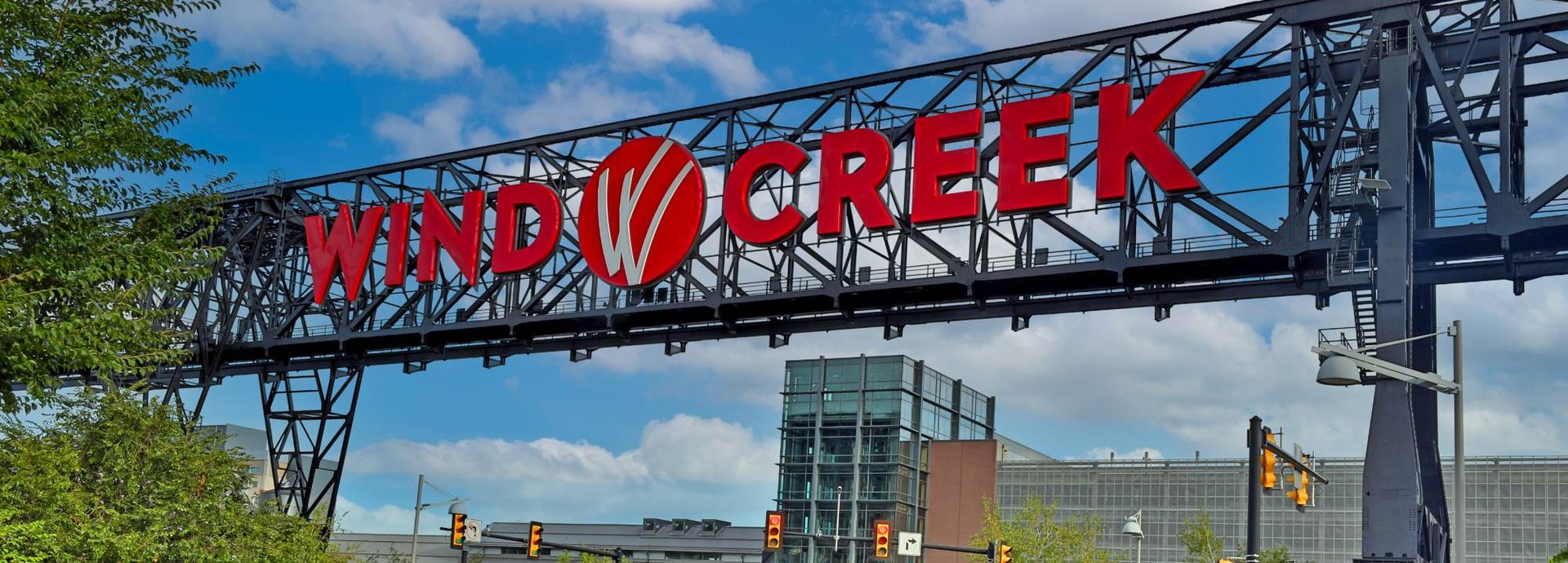 The red Wind Creek sign on the steel ore bridge over the entrance drive at Wind Creek Bethlehem, with the glass tower and casino behind